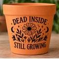 Orange plant pot with black flowers, crescent moons and Dead Inside Still Growing lettering