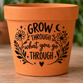 Orange plant pot with black flowers and Grow Through What You Go Through lettering